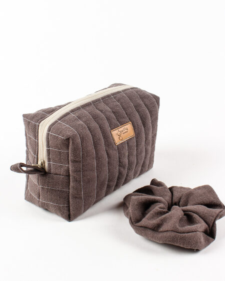 Ręcznie robiona brązowa lniana kosmetyczka z pasującą gumką scrunchie, umieszczona na białej teksturowanej powierzchni, w minimalistycznym stylu boho.