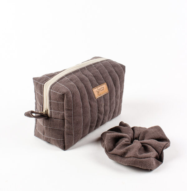 Ręcznie robiona brązowa lniana kosmetyczka z pasującą gumką scrunchie, umieszczona na białej teksturowanej powierzchni, w minimalistycznym stylu boho.