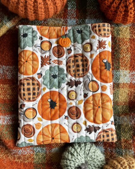 Jesienne pikowane etui na książkę z bawełny w dyniowy wzór. Miękkie book sleeve chroni książkę przed zarysowaniami i zagięciami podczas noszenia w torebce lub plecaku. Idealne dla miłośników jesieni, cozy reading i ręcznie szytych akcesoriów.