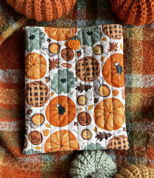 Jesienne pikowane etui na książkę z bawełny w dyniowy wzór. Miękkie book sleeve chroni książkę przed zarysowaniami i zagięciami podczas noszenia w torebce lub plecaku. Idealne dla miłośników jesieni, cozy reading i ręcznie szytych akcesoriów.