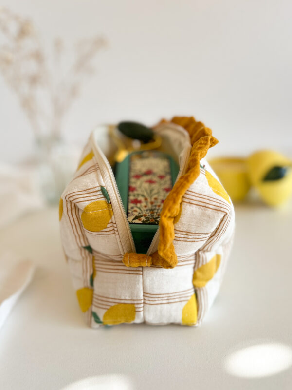 Ręcznie wykonana kosmetyczka w cytrynki trzymana w dłoni, pokazująca rozmiar pikowanej bawełnianej saszetki z falbanką.