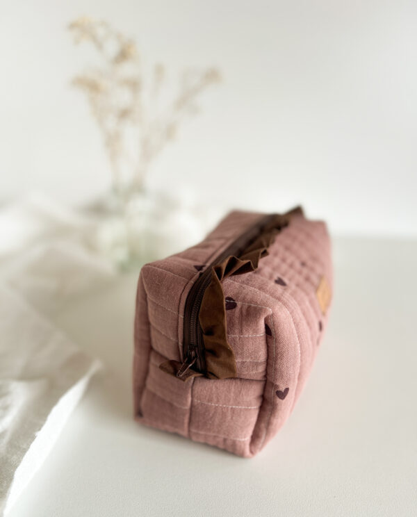 Ręcznie wykonana kosmetyczka w serduszka trzymana w dłoni, pokazująca rozmiar pikowanej bawełnianej saszetki z falbanką.