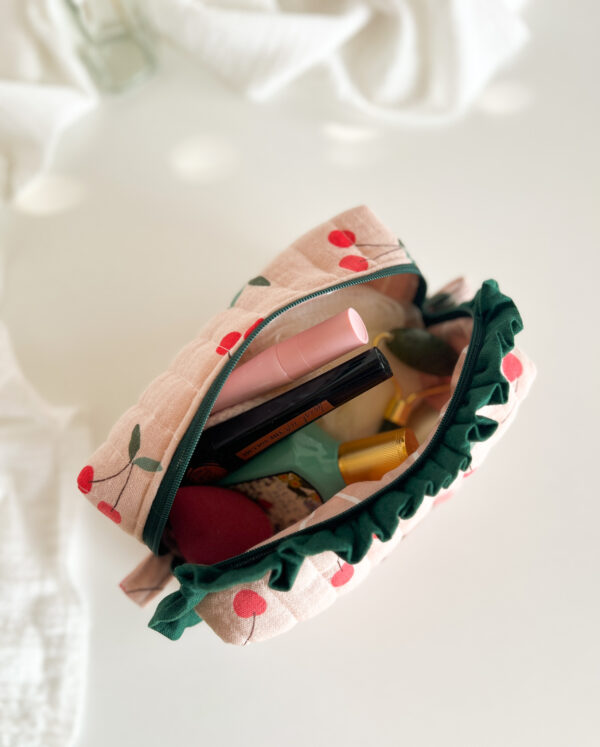 Pikowana kosmetyczka w czereśnie ustawiona na toaletce, dekoracyjna saszetka na kosmetyki w kobiecym stylu.