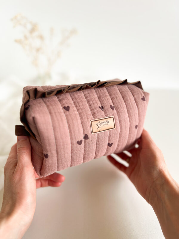 Kosmetyczka w serduszka z falbanką ustawiona na toaletce, dekoracyjna saszetka na makijaż w dziewczęcym stylu.