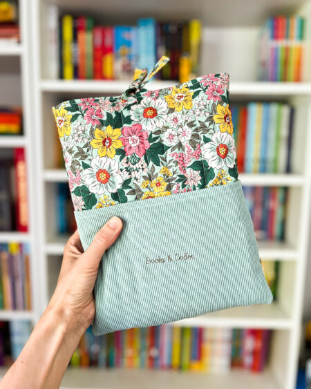 Kwiatowe etui na książkę z miętowym sztruksem i haftem „Books & Coffee”, sfotografowane obok pastelowych długopisów.