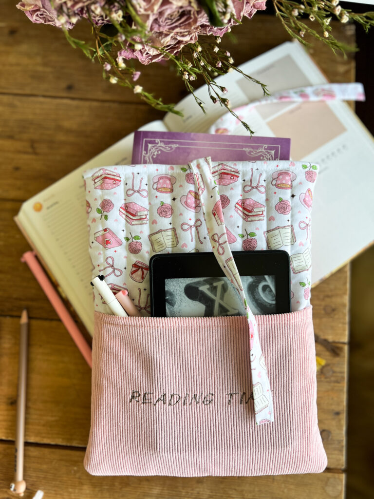 Ręcznie wykonane różowe etui na książkę z motywem książek, herbaty i kwiatów oraz haftem „Reading Time”.
