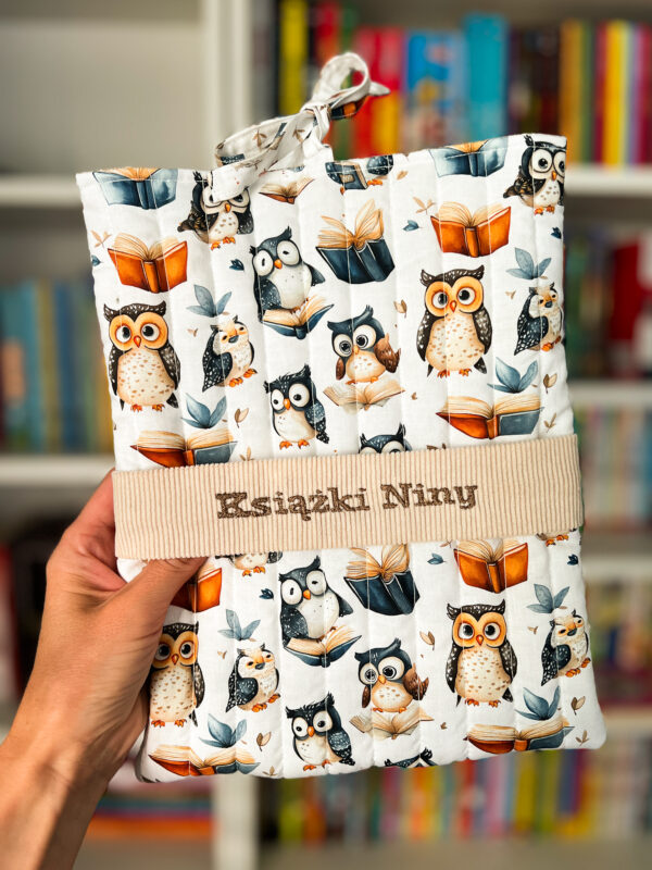 Personalizowane etui na książkę z haftowanym napisem „Książki Niny”, pikowane etui z motywem sów i książek chroniące książkę przed zniszczeniem.