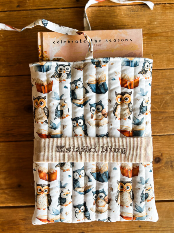 Zbliżenie na personalizowane etui na książkę z haftem oraz bawełnianym wzorem w sowy i książki.