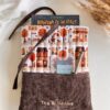 Ręcznie szyte book sleeve z jesiennym wzorem przedstawiającym małe kawiarnie, księgarnię, rowery i jesienne drzewa. Brązowy sztruks ozdobiony jest haftem Tea & Books, a z etui wystaje książka.