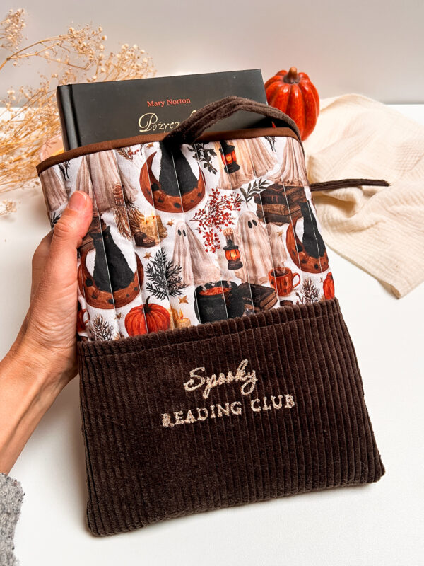 Ręcznie szyte brązowe etui na książkę Spooky Reading Club z kieszonką, jesiennym wzorem książek, dyń i czarnych kotów.